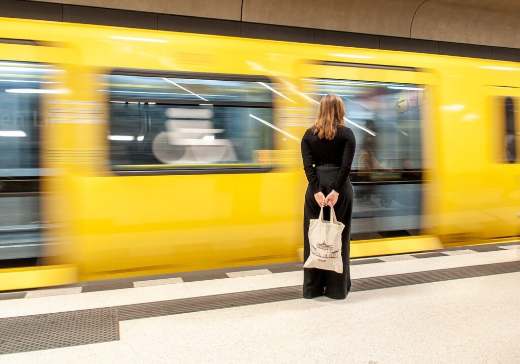 高速で通りすぎる黄色い電車を見つめる黒い服を来た金髪の女性